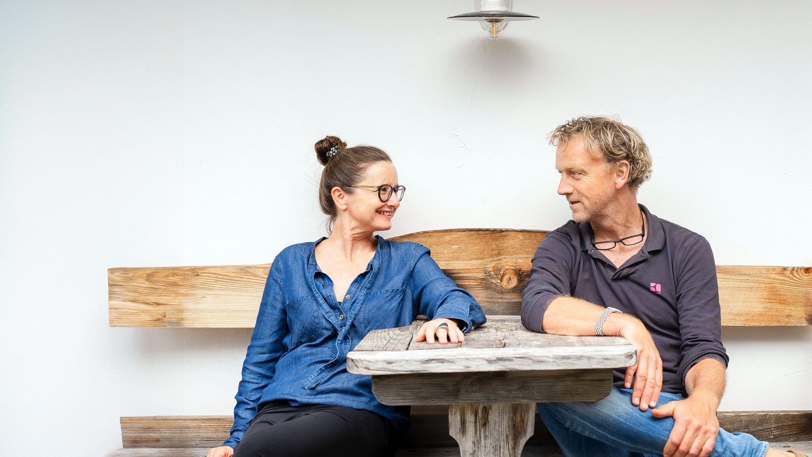 Eine Frau und ein Mann sitzen auf einer Holzbank an einem Tisch und schauen sich an.
