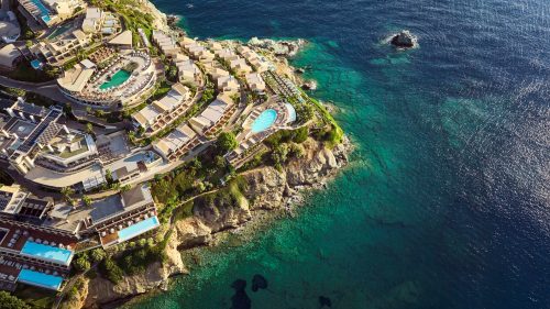 Luftaufnahme des Seaside Lifestyle Resorts auf Kreta, das an einer Klippenkante mit Blick auf das klare, türkisfarbene Wasser liegt.