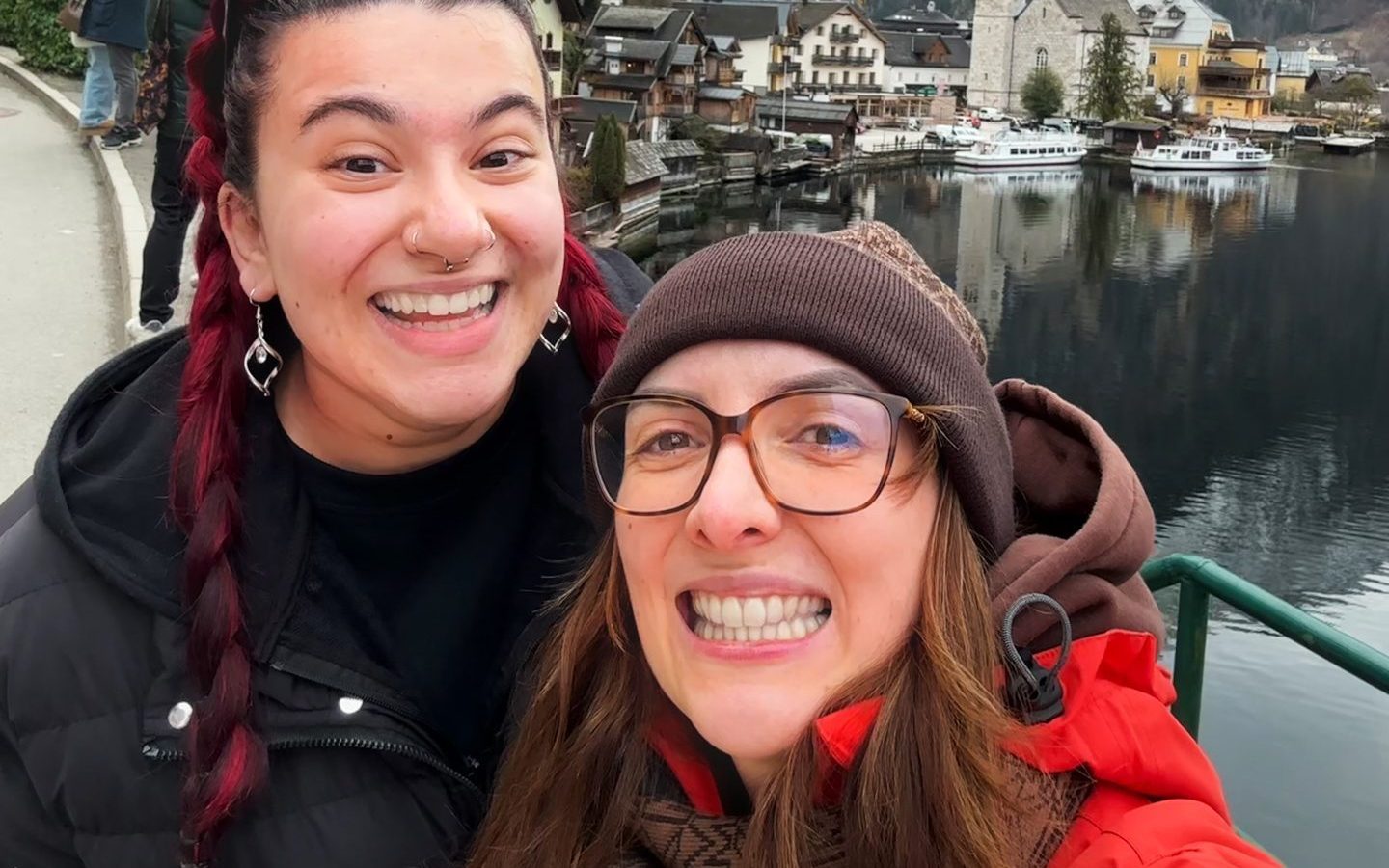 Zwei Frauen lächeln für ein Selfie vor einem See und verschneiten Berglandschaften.