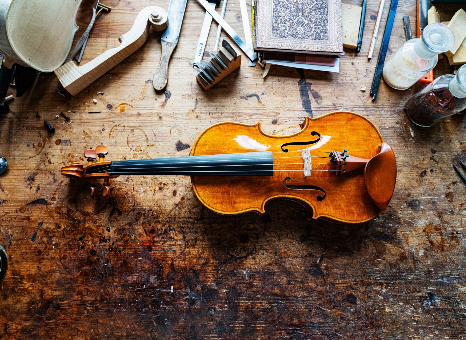 Eine Violine liegt auf einer mit Werkzeugen und Materialien gefüllten Werkbank.