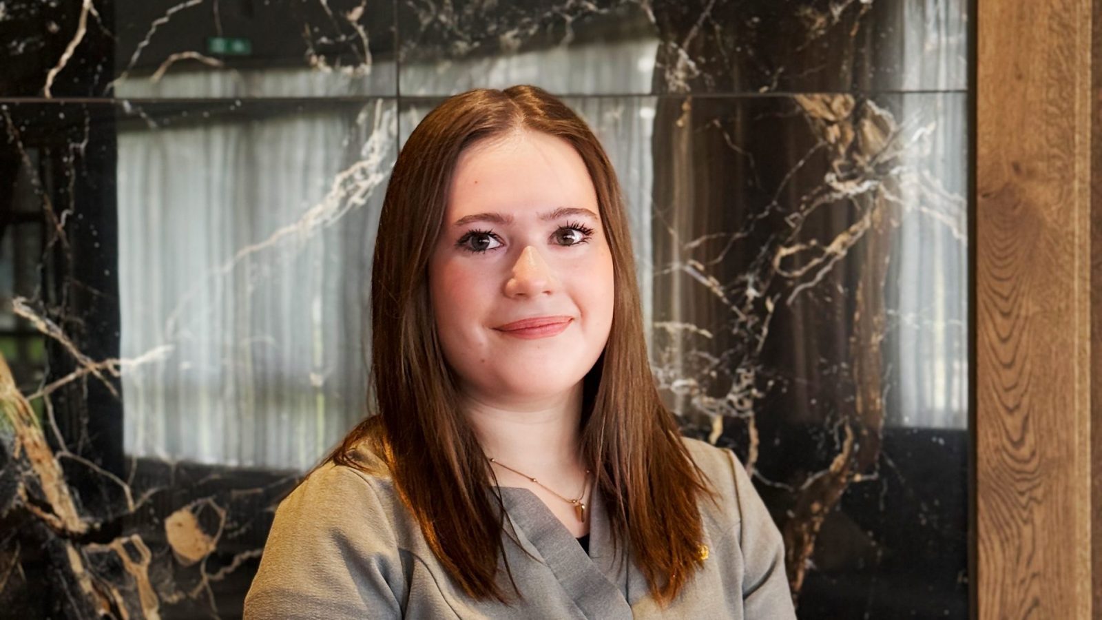 Porträt einer jungen Frau in einer hellbraunen Bluse vor einer marmorierten Wand.