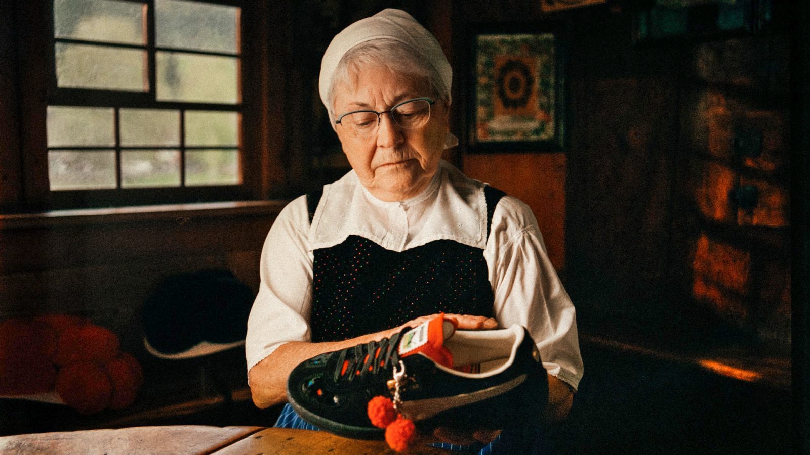 Eine Bollenhutmacherin betrachtet einen „Bollenhut“-Schuh von Puma in einem Holzraum. Auf dem Tisch liegen eine Schere und Stoffstücke.